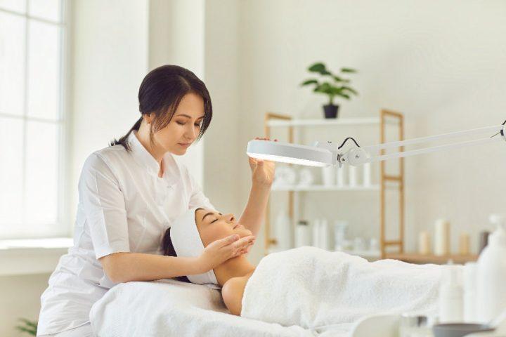 A certified dermatologist examines a client’s skin to prepare for a facial beauty treatment.